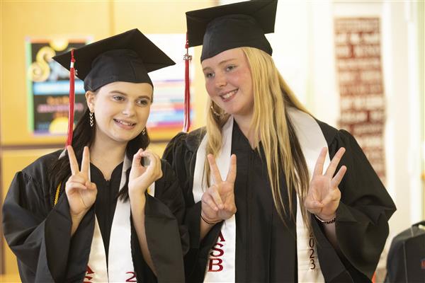 Two girls wearing caps and gowns hold up their fingers to indicate \